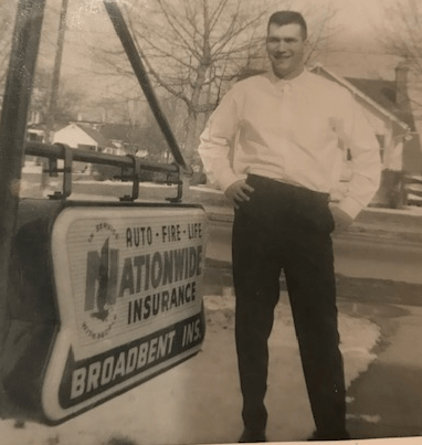 Man standing in front of a Nationwide Insurance sign. He's wearing a white shirt and dark pants. Snowy setting.