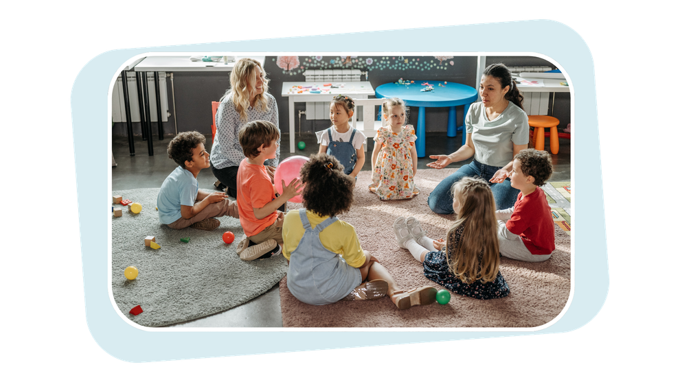 Children sitting in a circle on a rug, playing and talking in a bright classroom