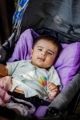 Baby lying in a purple stroller, wearing a light shirt and looking at the camera