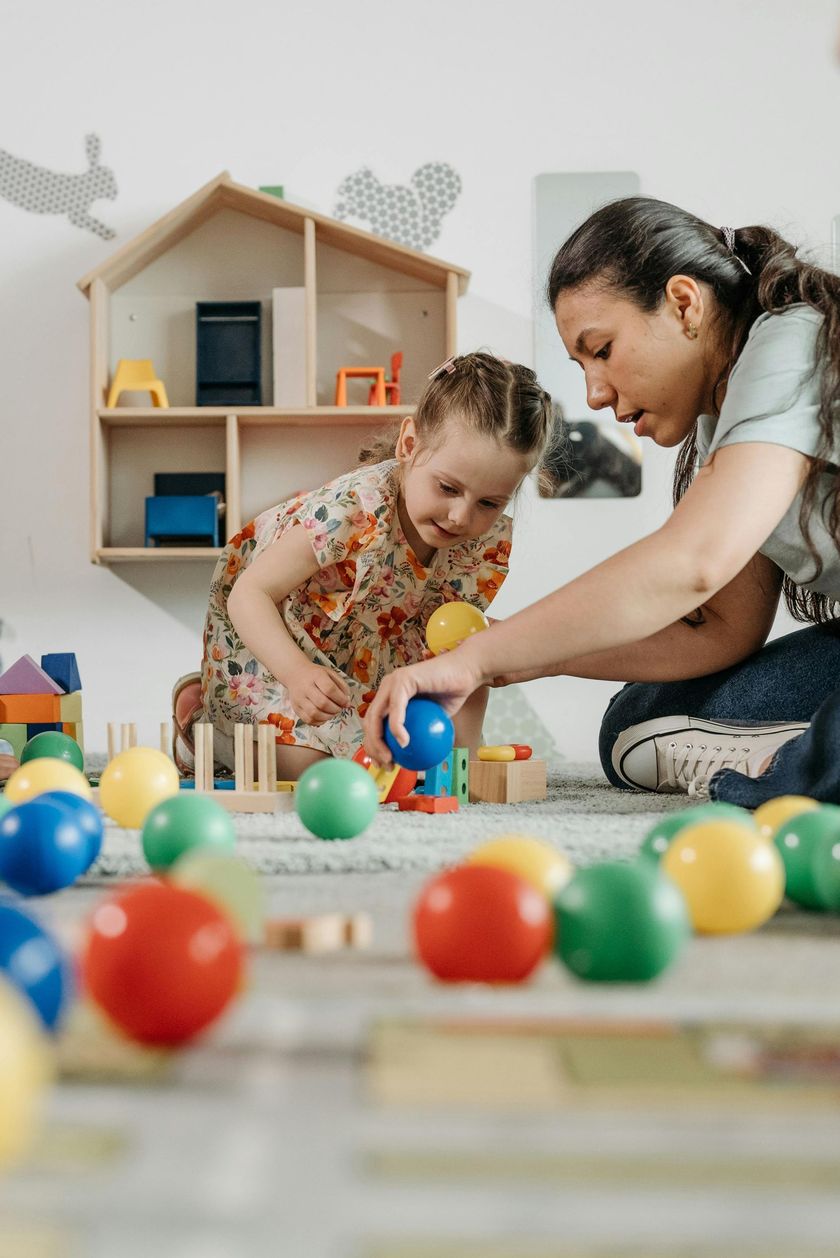 Two people playing with colorful balls on the floor in a bright playroom