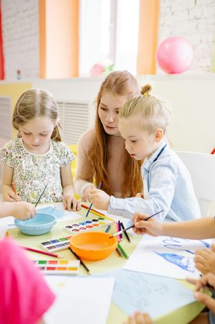 Children painting at a table with colorful art supplies in a bright classroom