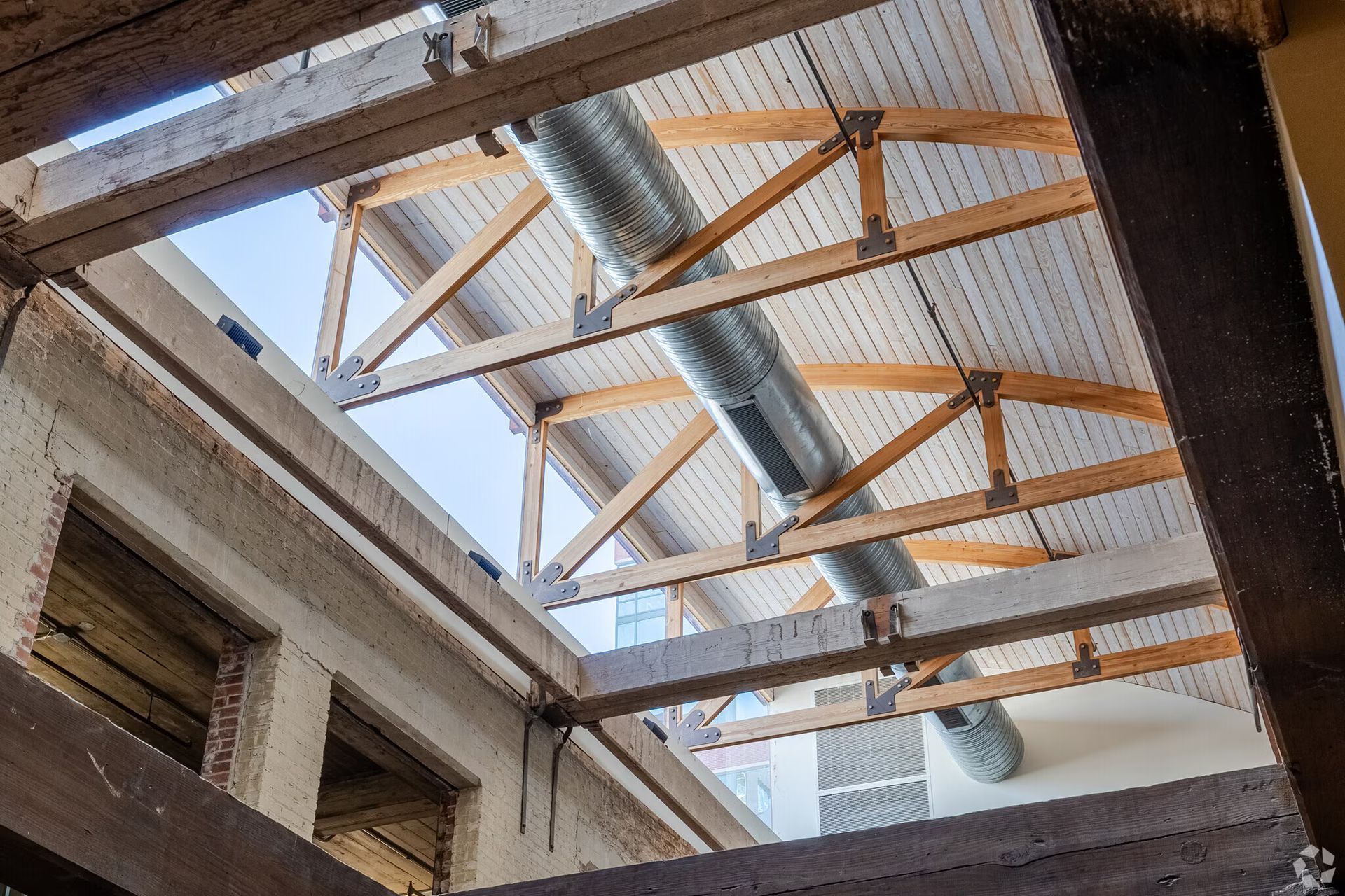 Interior view of a building with exposed wooden roof trusses, skylight, and ventilation ductwork.