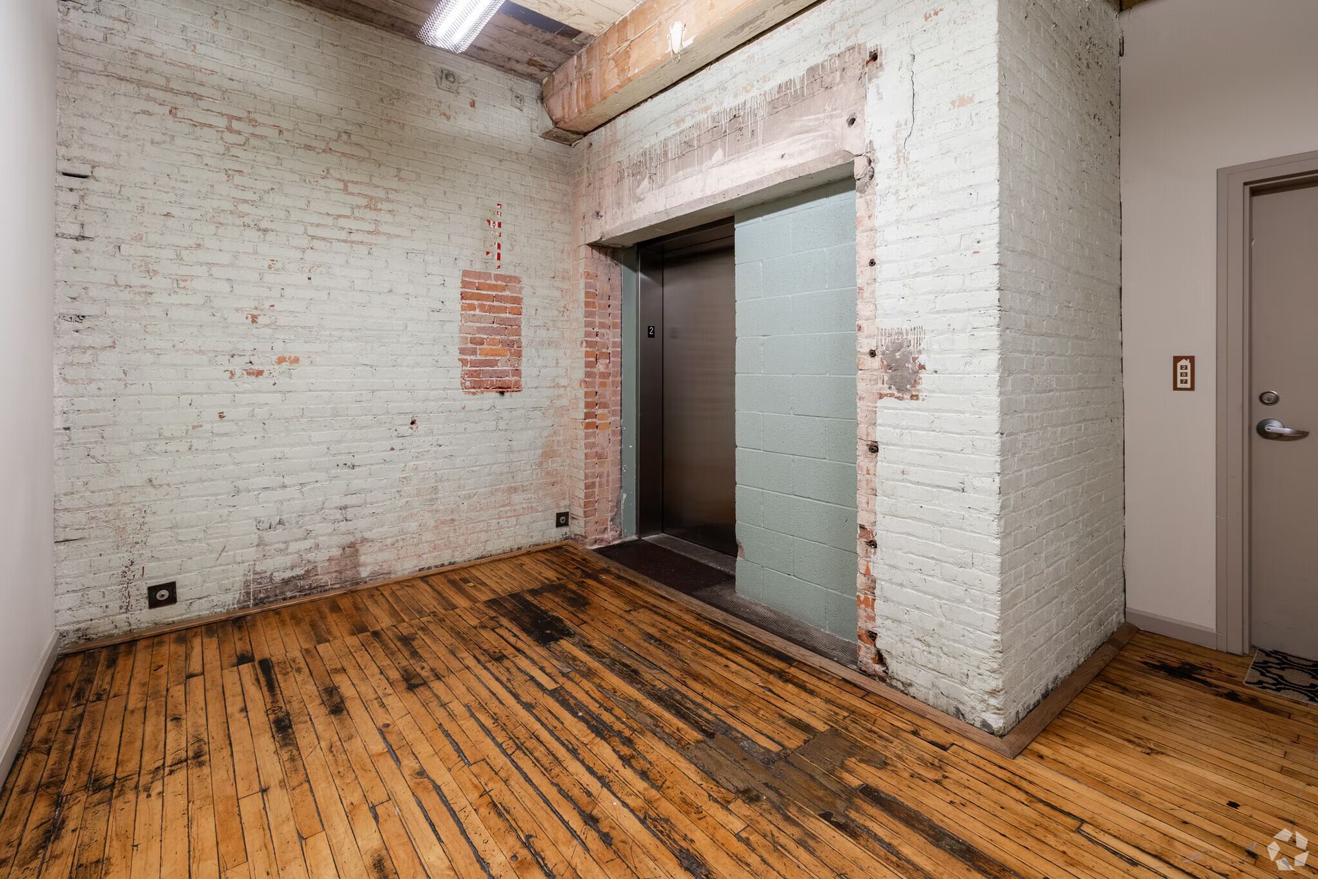 Empty room with exposed brick and wooden floor, open elevator.