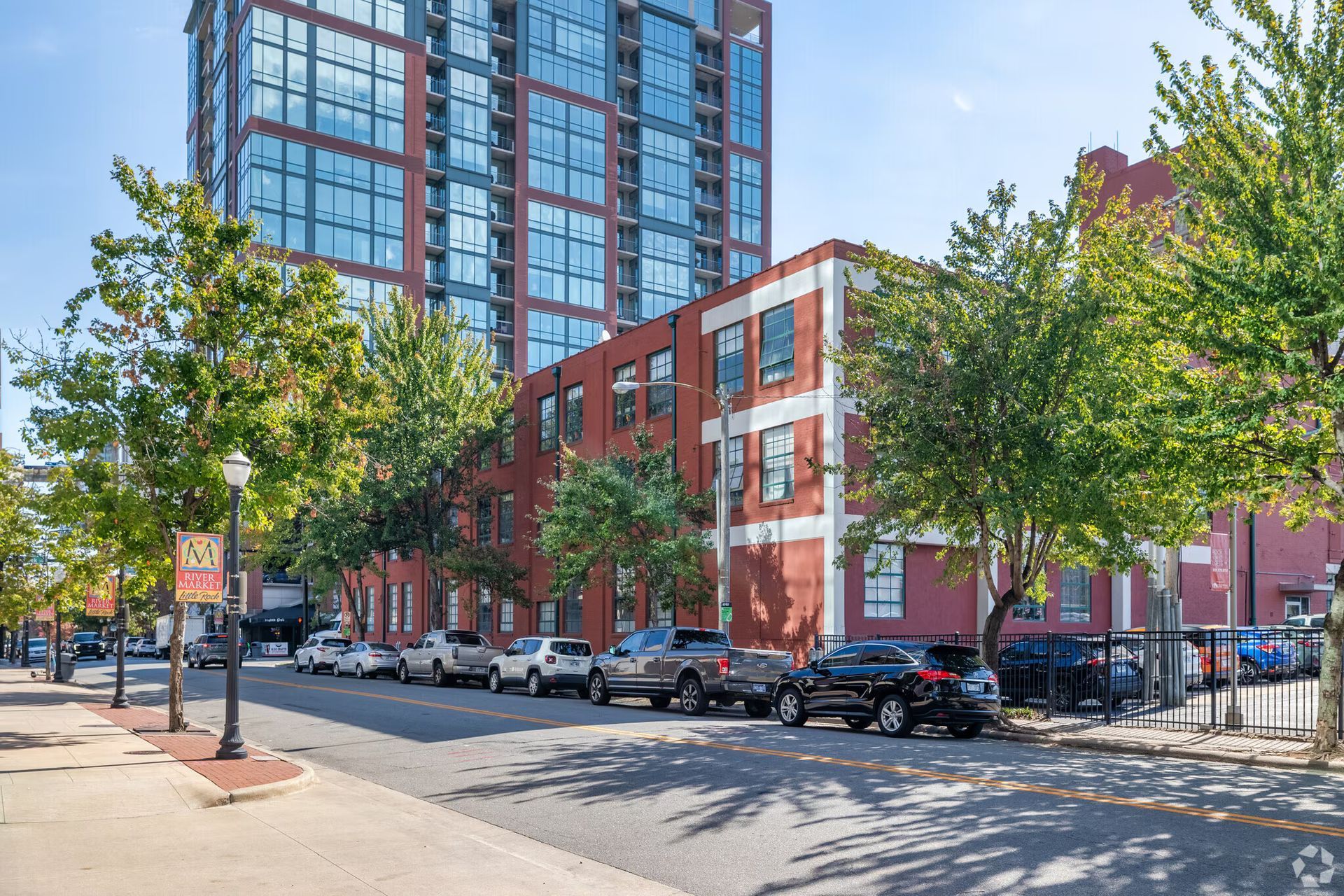 Street view with cars parked on both sides, red brick building, and modern high-rise.