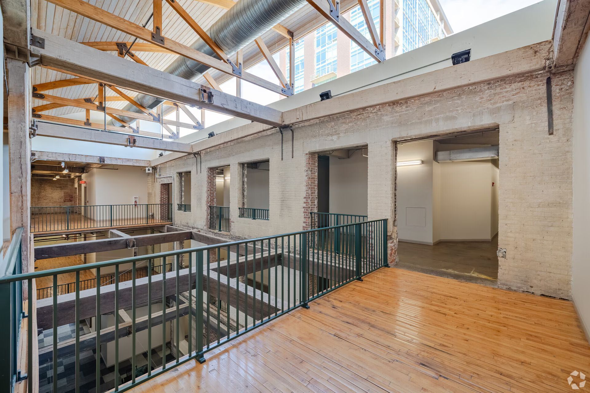Interior of an open-concept loft with exposed brick, wooden beams, and a second-story walkway.
