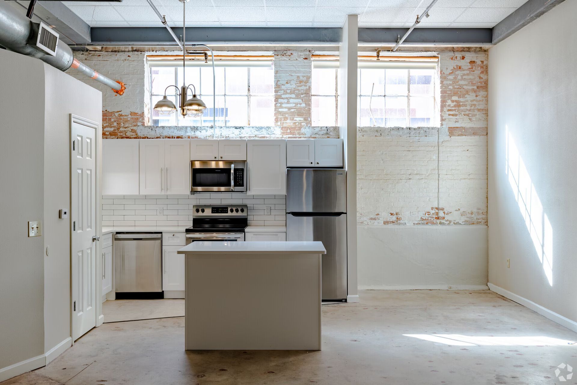Modern kitchen with white cabinets, stainless steel appliances, and exposed brick walls.
