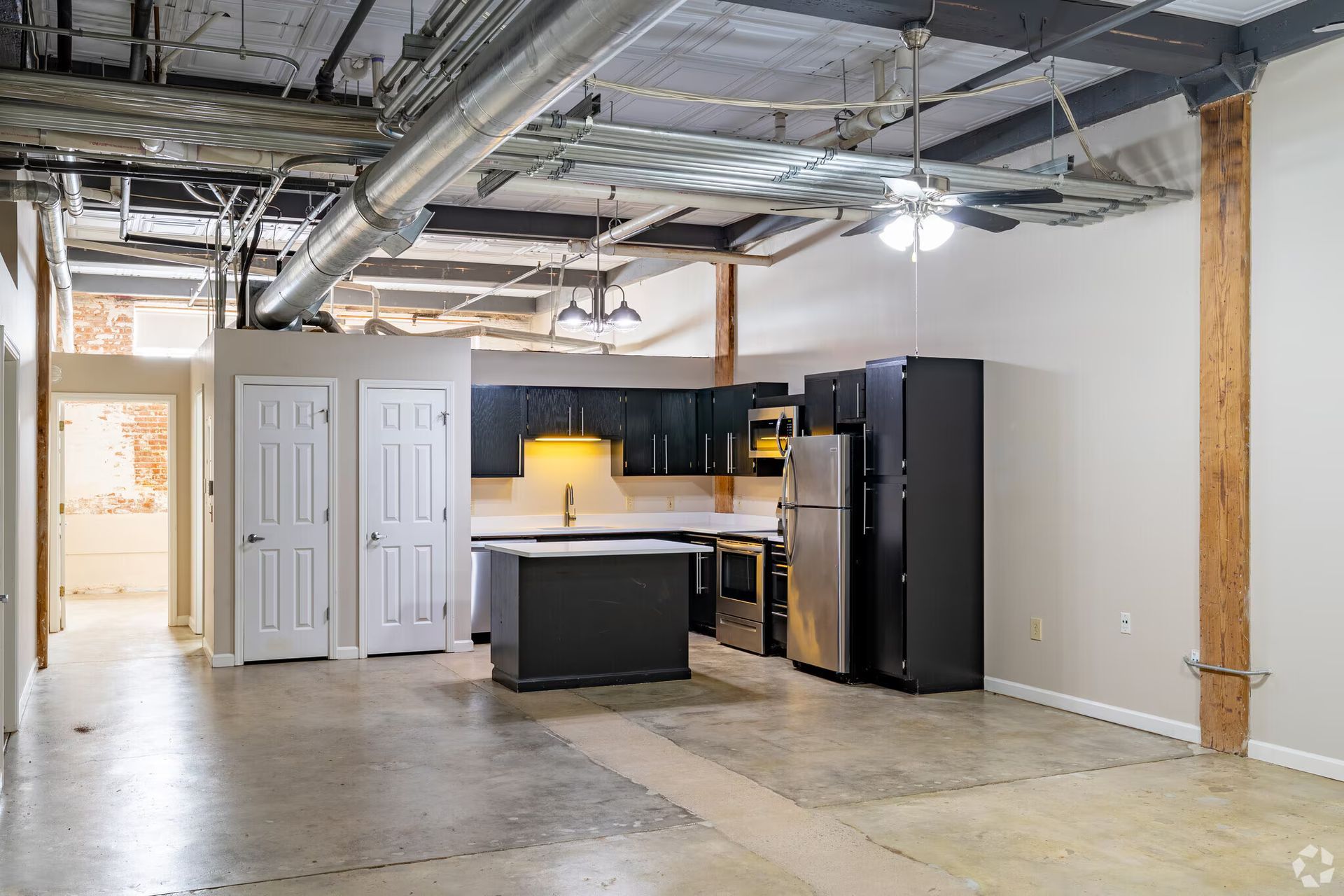 Loft apartment with exposed ductwork, kitchen with black cabinets and island, concrete floor, wooden support beam.