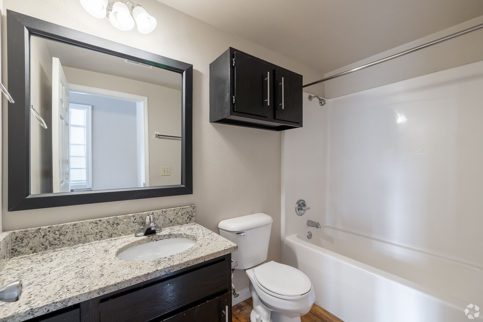 Bathroom with vanity, toilet, tub, black cabinets, and large mirror.