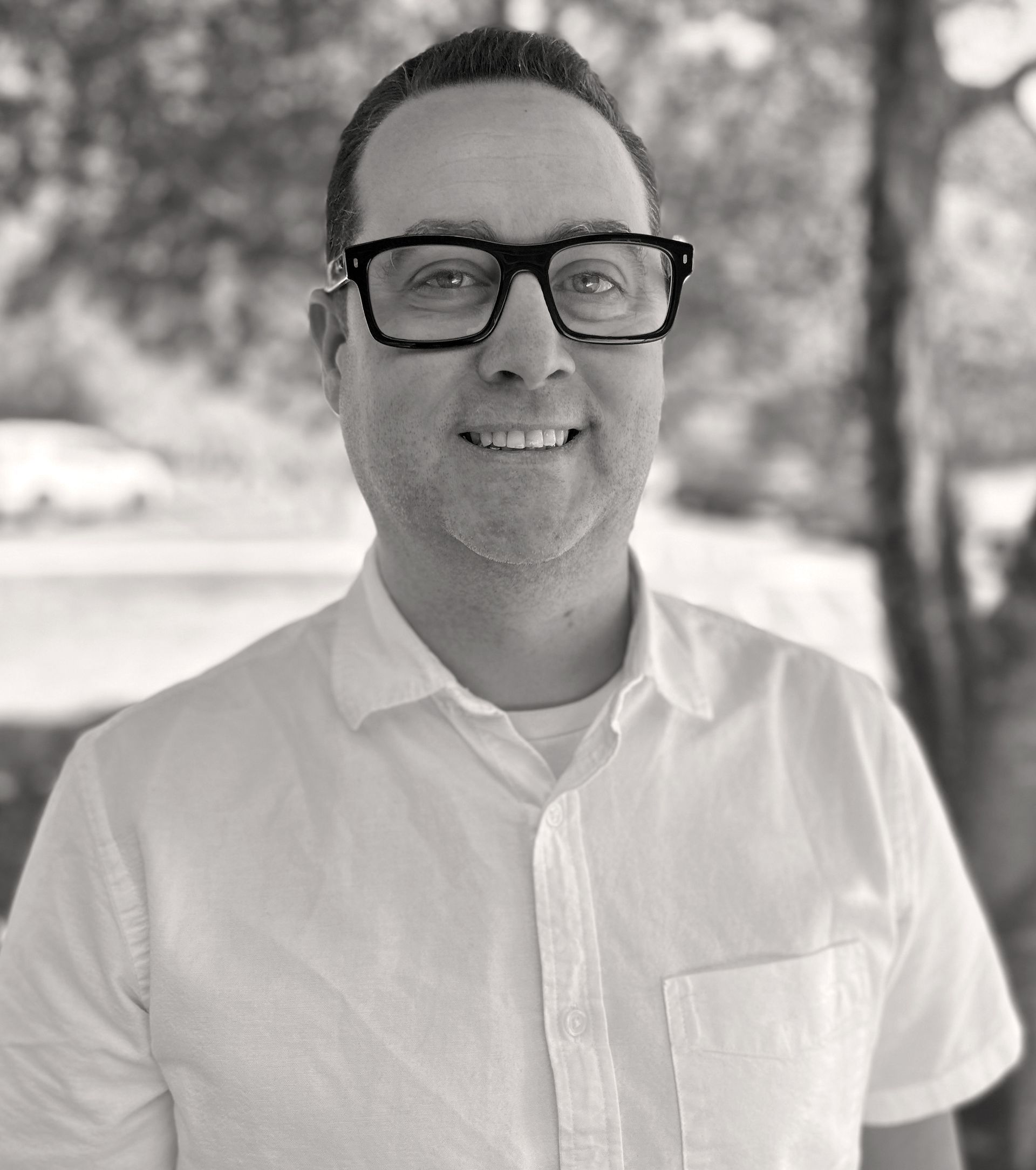 Man wearing glasses smiling, in white shirt, headshot. Brett Coppenger