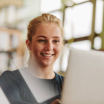 Person in red shirt seated on a rooftop, reading a book. Surrounded by plants, city buildings in background.