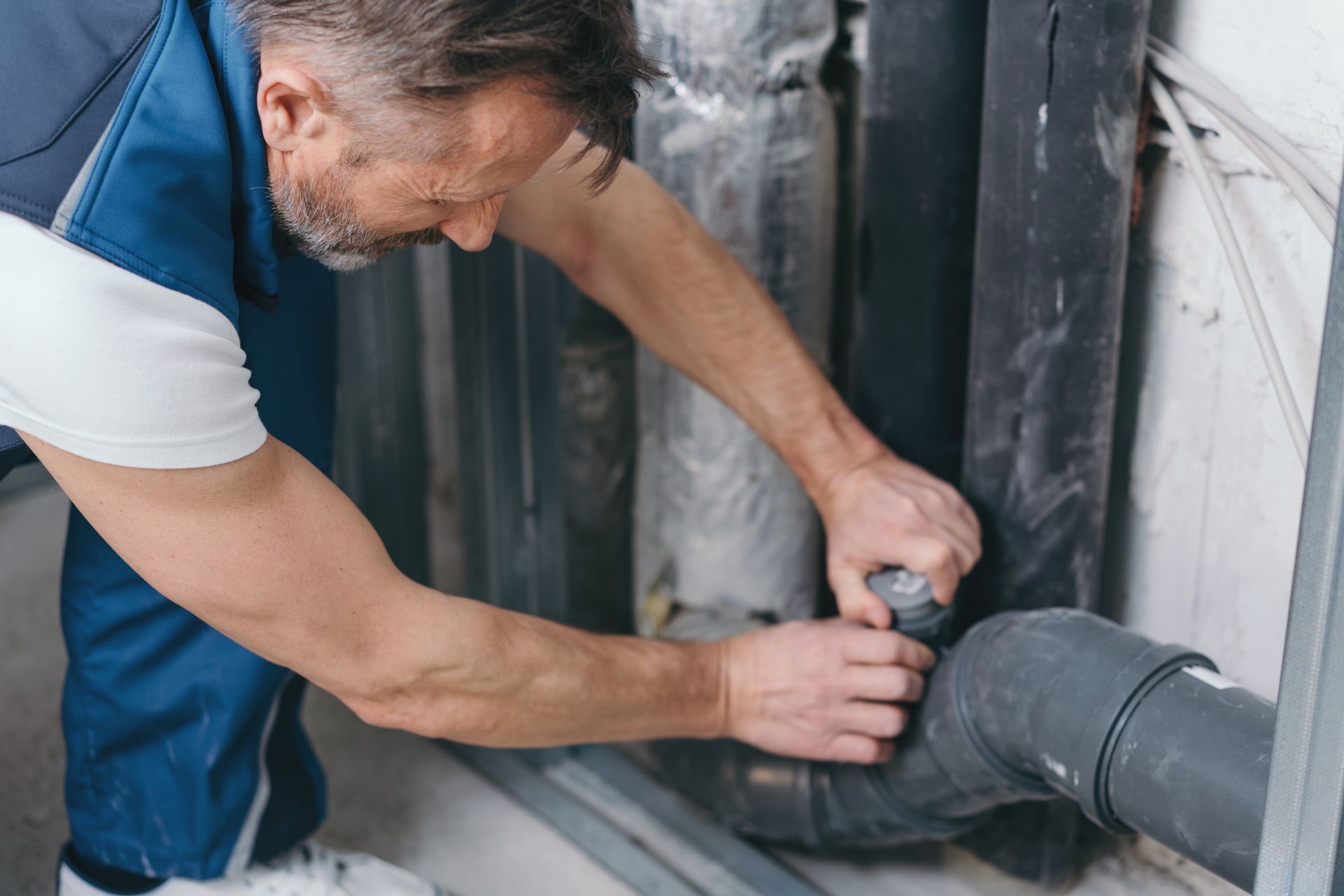 Plumber working on black pipes in a utility room