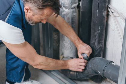 Plumber working on black pipes in a utility room
