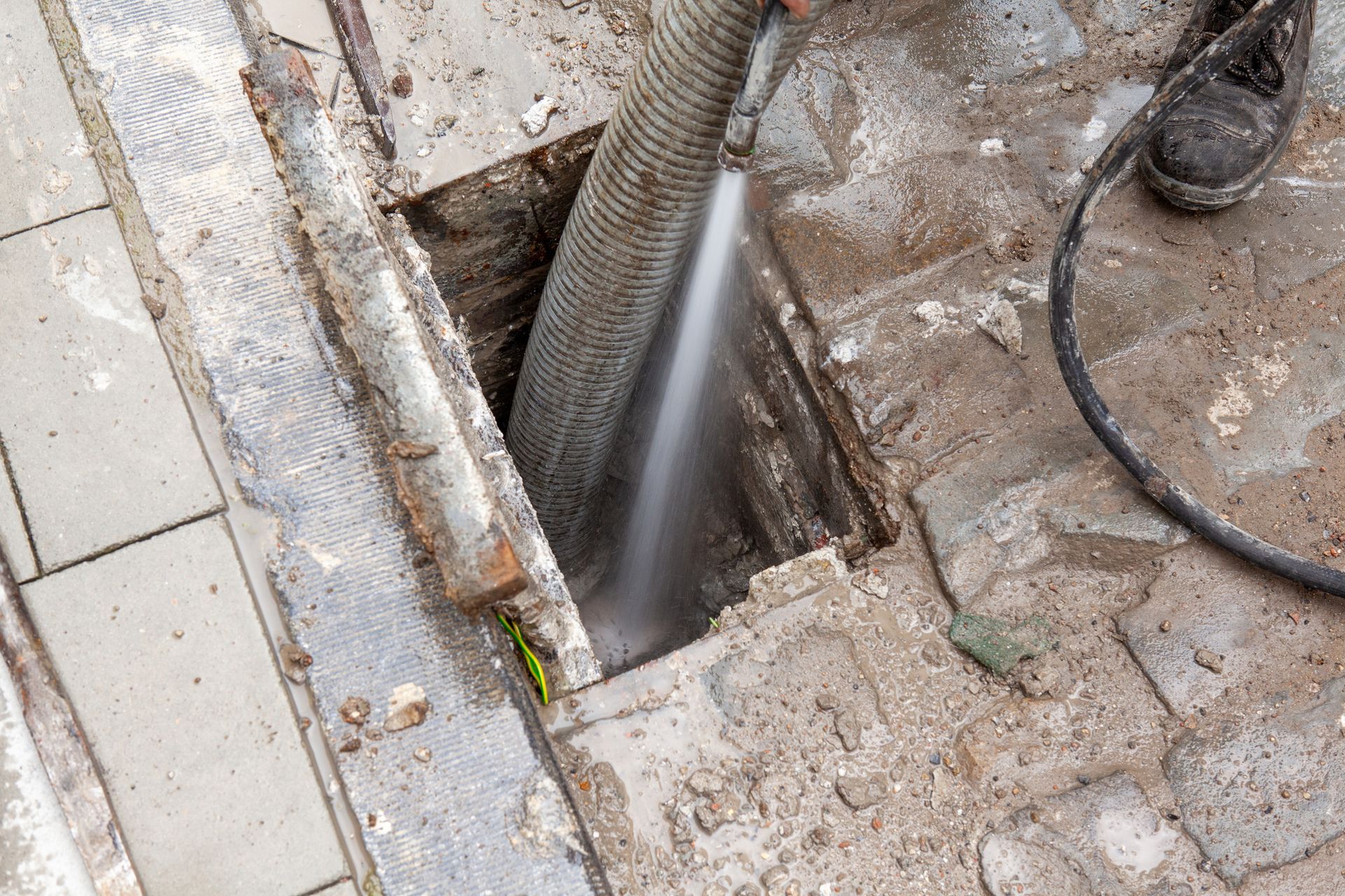 A person using high-pressure water in an open sewer A person using high-pressure water in an open sewer