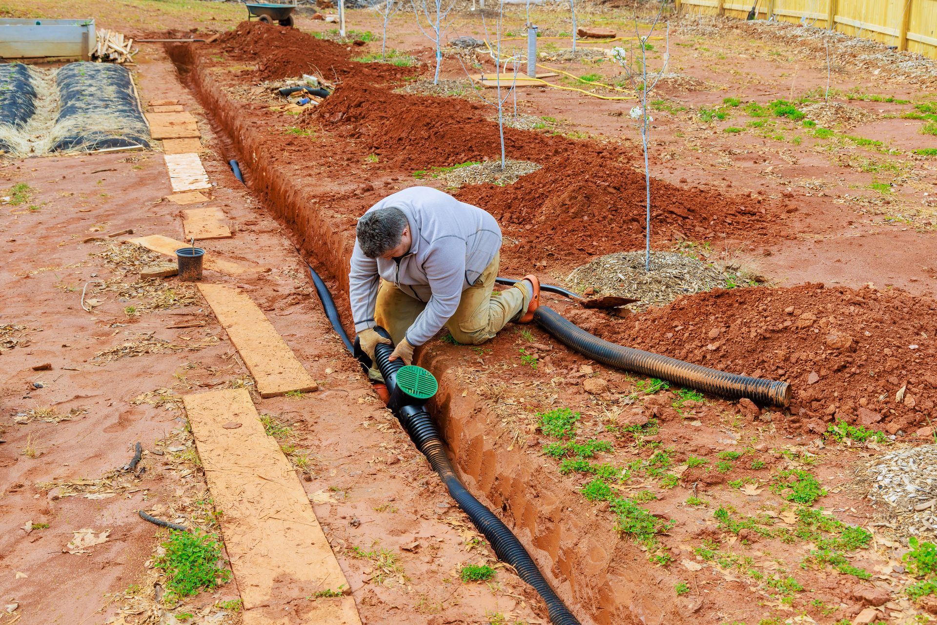 Man installing drainage pipe in a trench in a garden Man installing drainage pipe in a trench in a garden