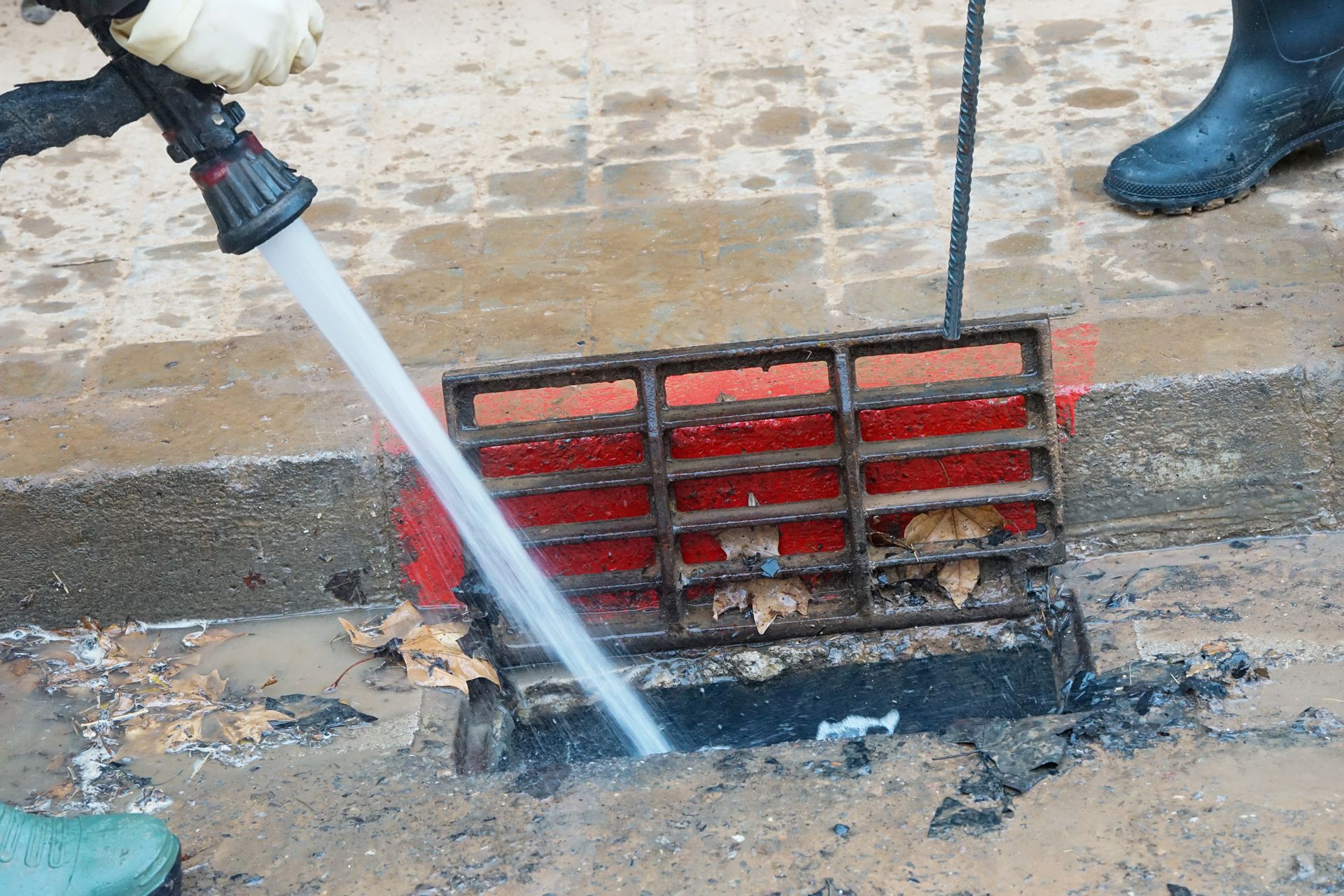Person cleaning a street drain with a water hose, removing debris Person cleaning a street drain with a water hose, removing debris