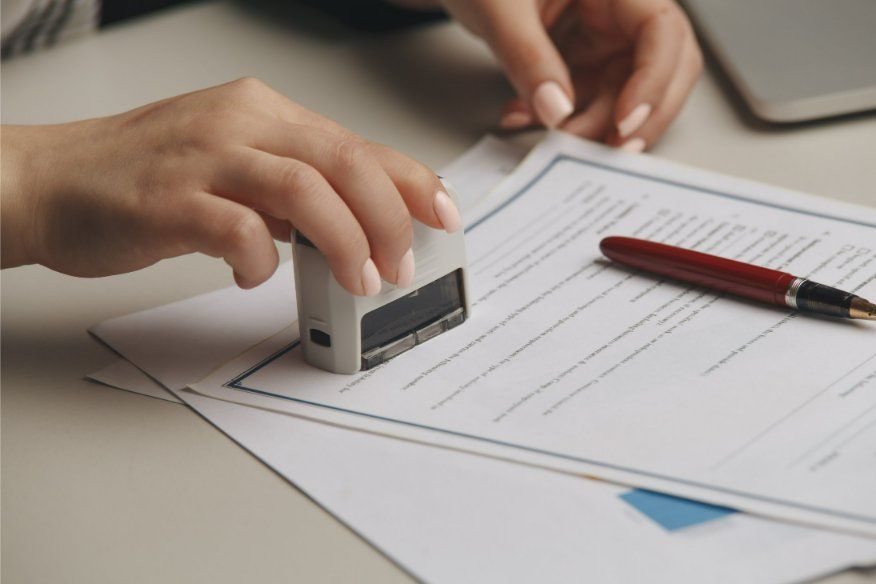 Person stamps a document with a rectangular stamp on a desk with a pen and other papers.