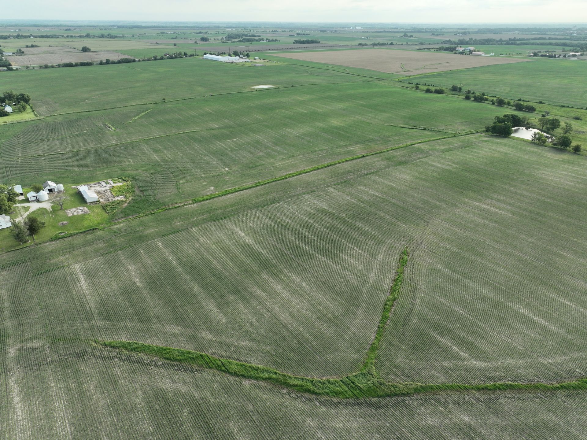 An aerial view of a lush green field with a house in the distance