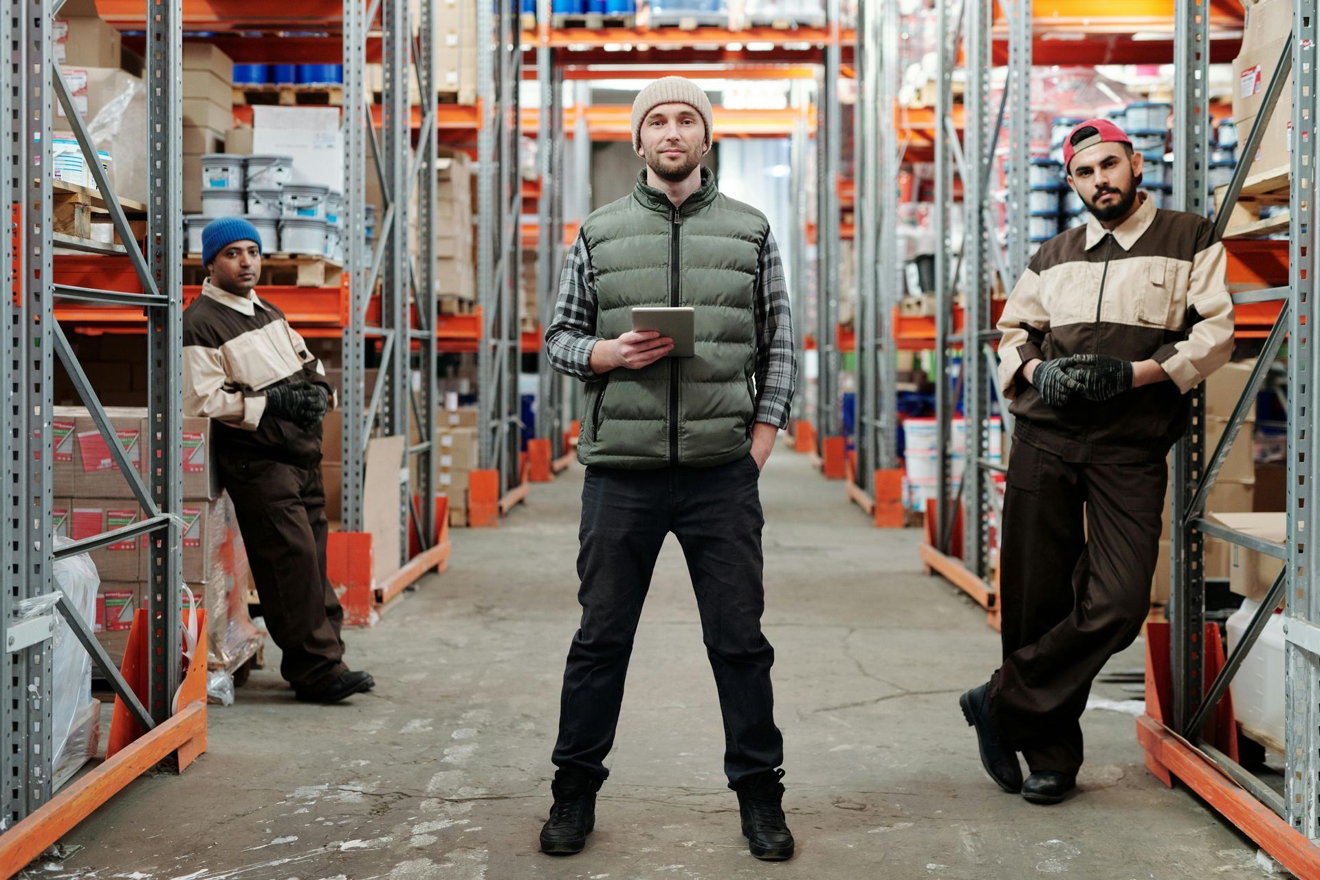 Three men are standing in a warehouse holding a tablet.
