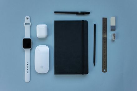A black notebook , a white watch , a mouse , a pen , and a ruler on a blue surface.