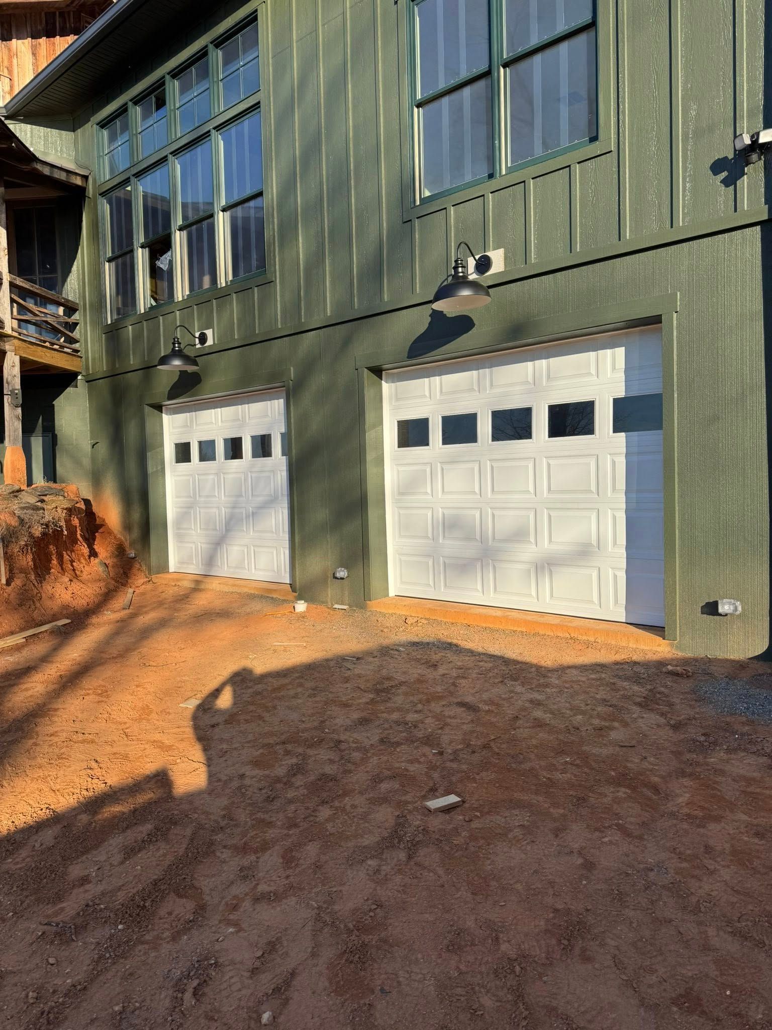 Green building facade with two white garage doors and large windows on a dirt lot