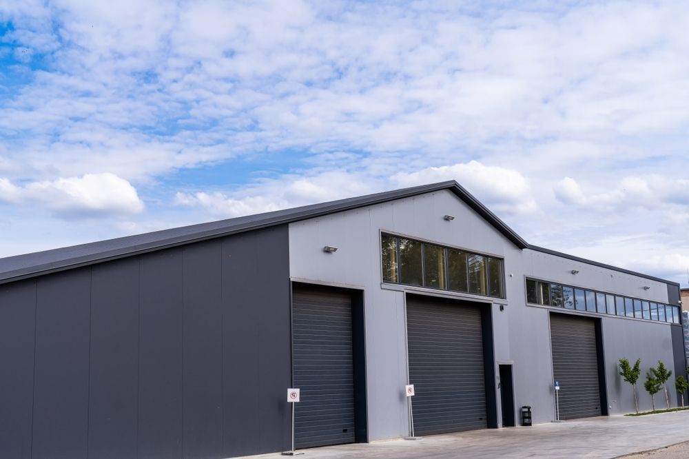 Modern gray industrial warehouse with roll-up doors under a cloudy sky