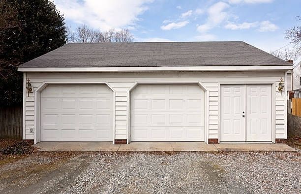 Three-car white garage with two large doors and a side entry door on a gravel driveway