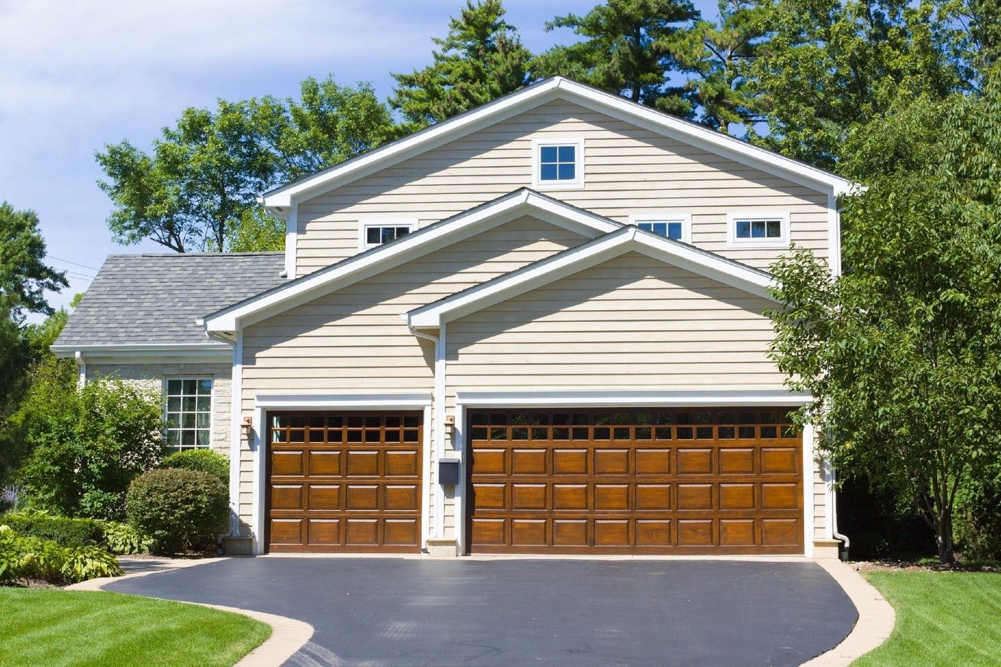 Suburban house with two wooden garage doors, white siding, and a driveway under blue sky