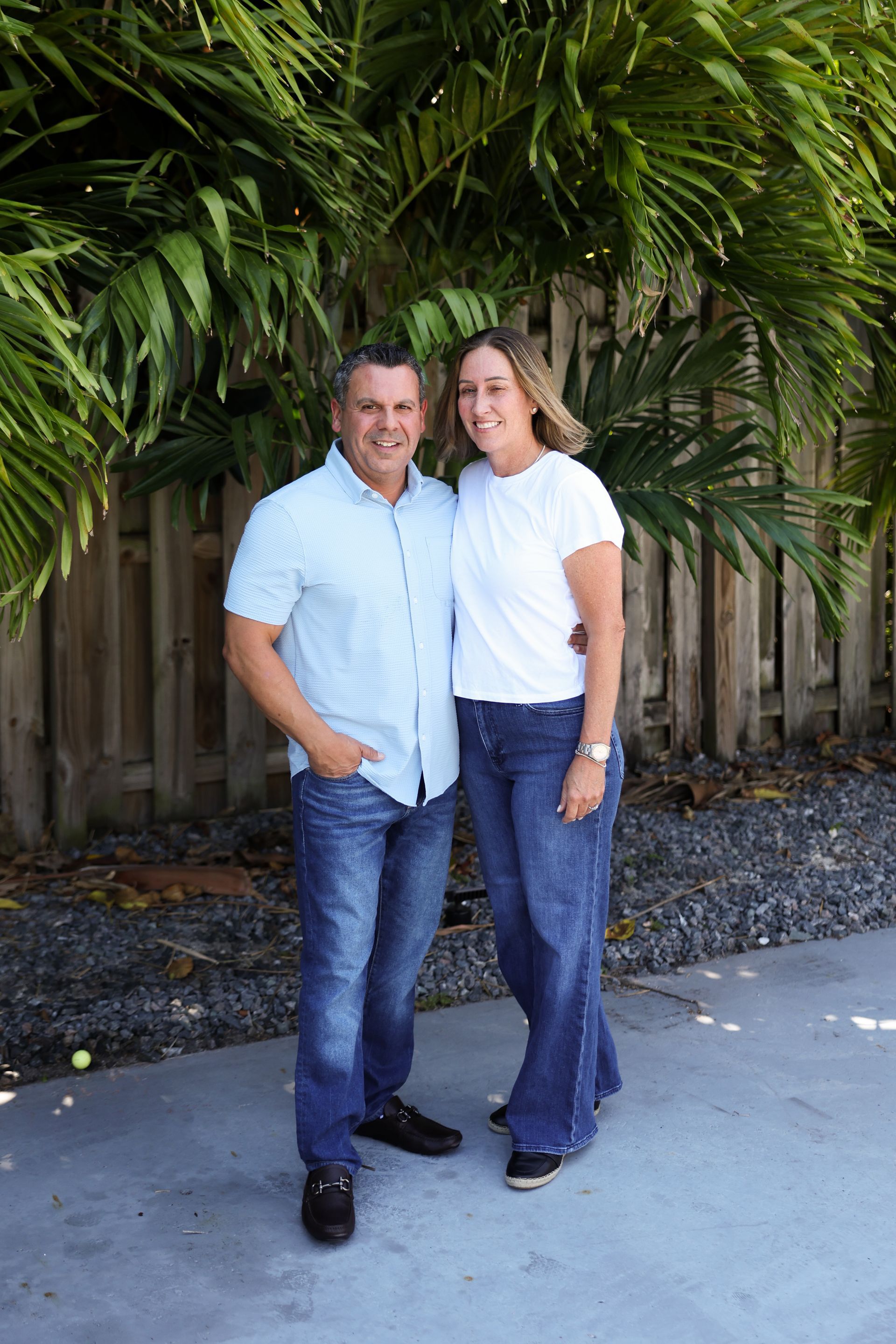 A man and a woman are posing for a picture in front of a fence.