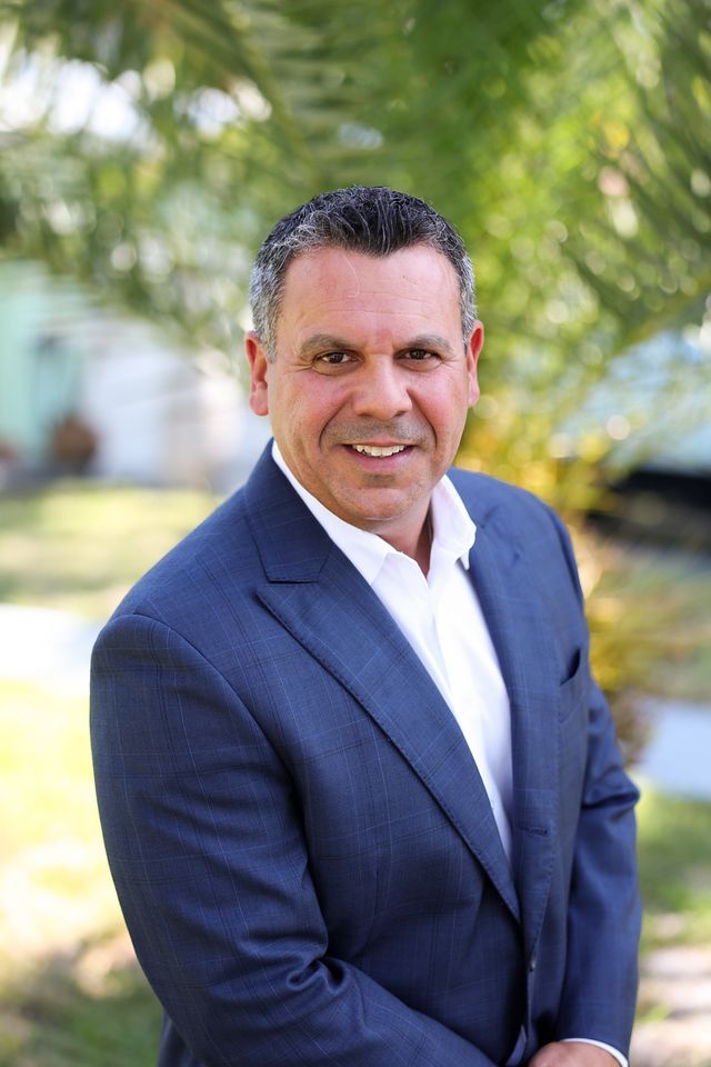 A man in a suit and white shirt is smiling for the camera.