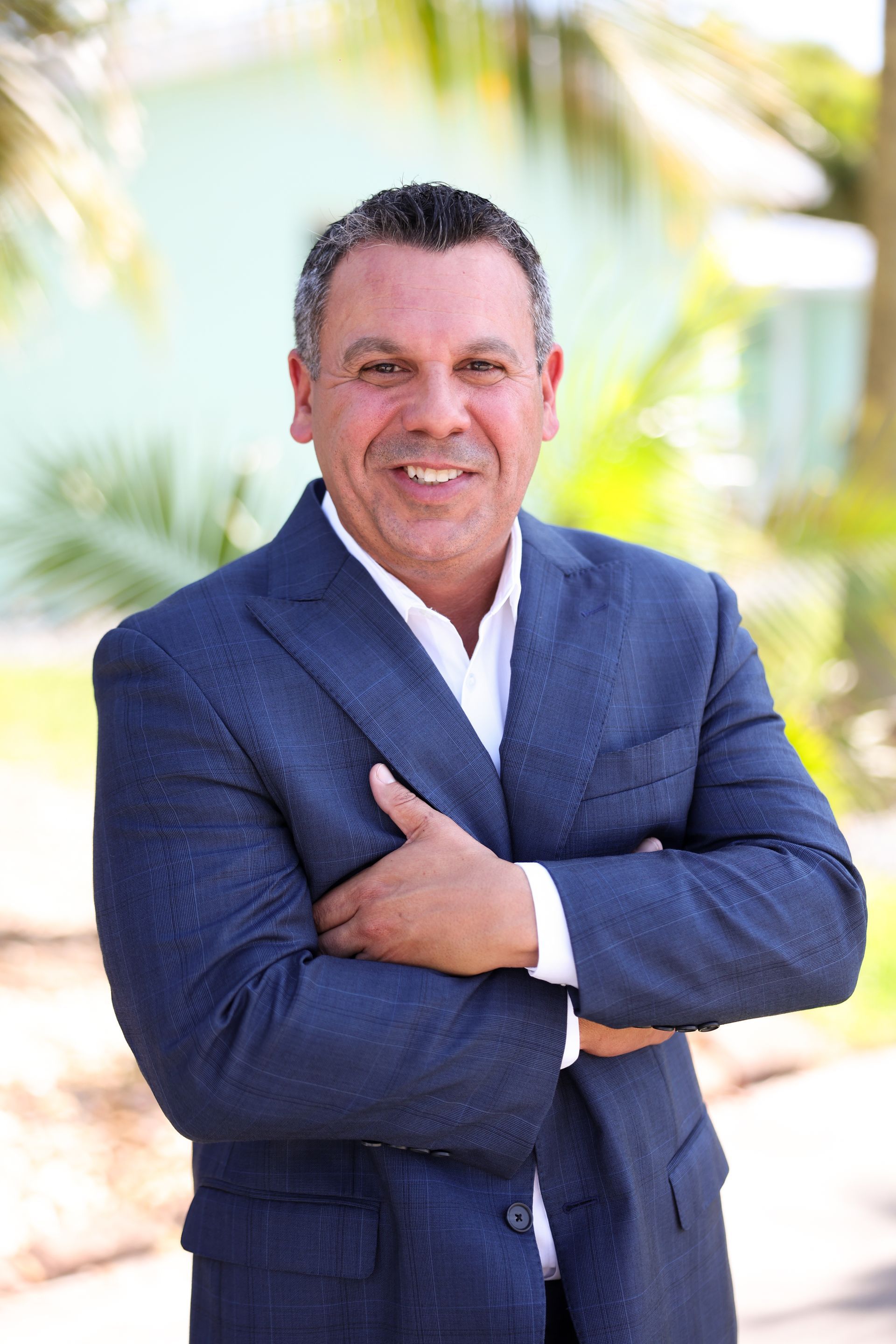 A man in a suit is standing with his arms crossed and smiling.