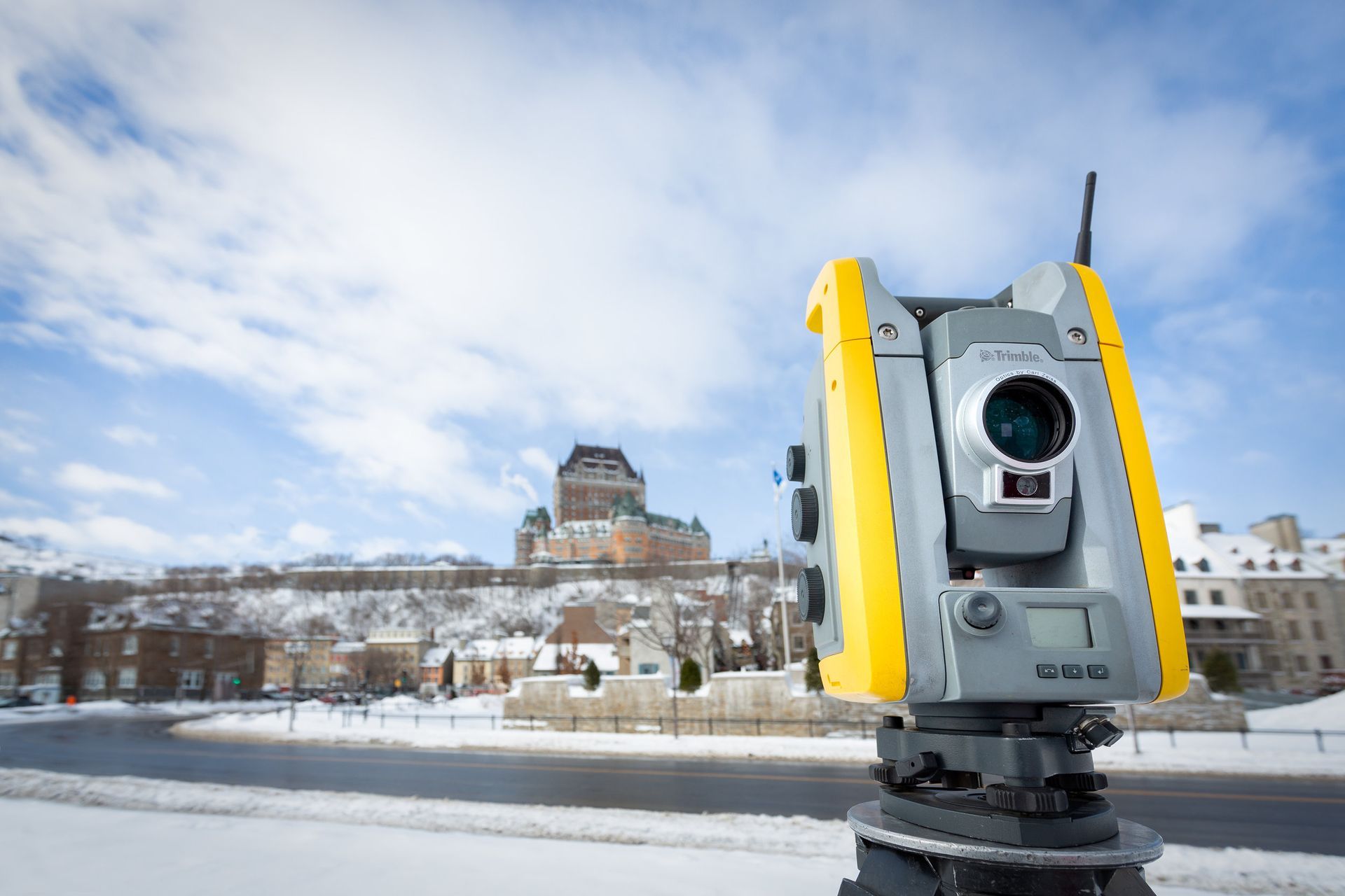 Un théodolite jaune et gris est posé dans la neige devant un bâtiment.