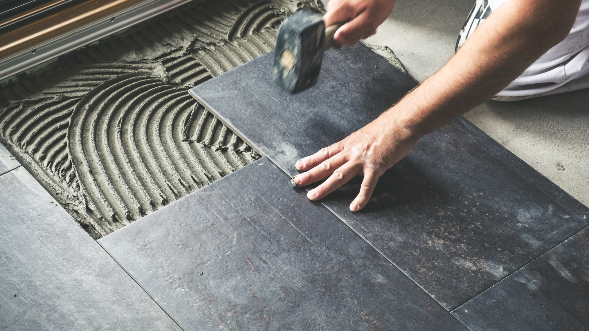 A person is laying tiles on the floor with a trowel.