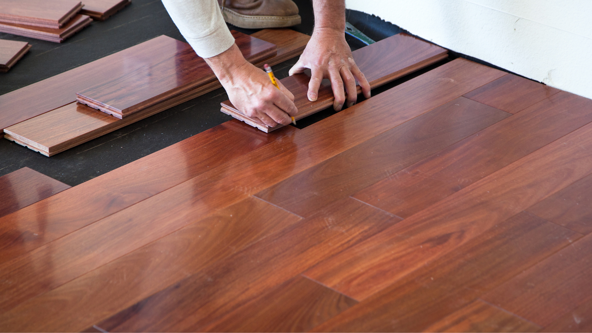 A person is measuring a piece of wood on a hardwood floor.