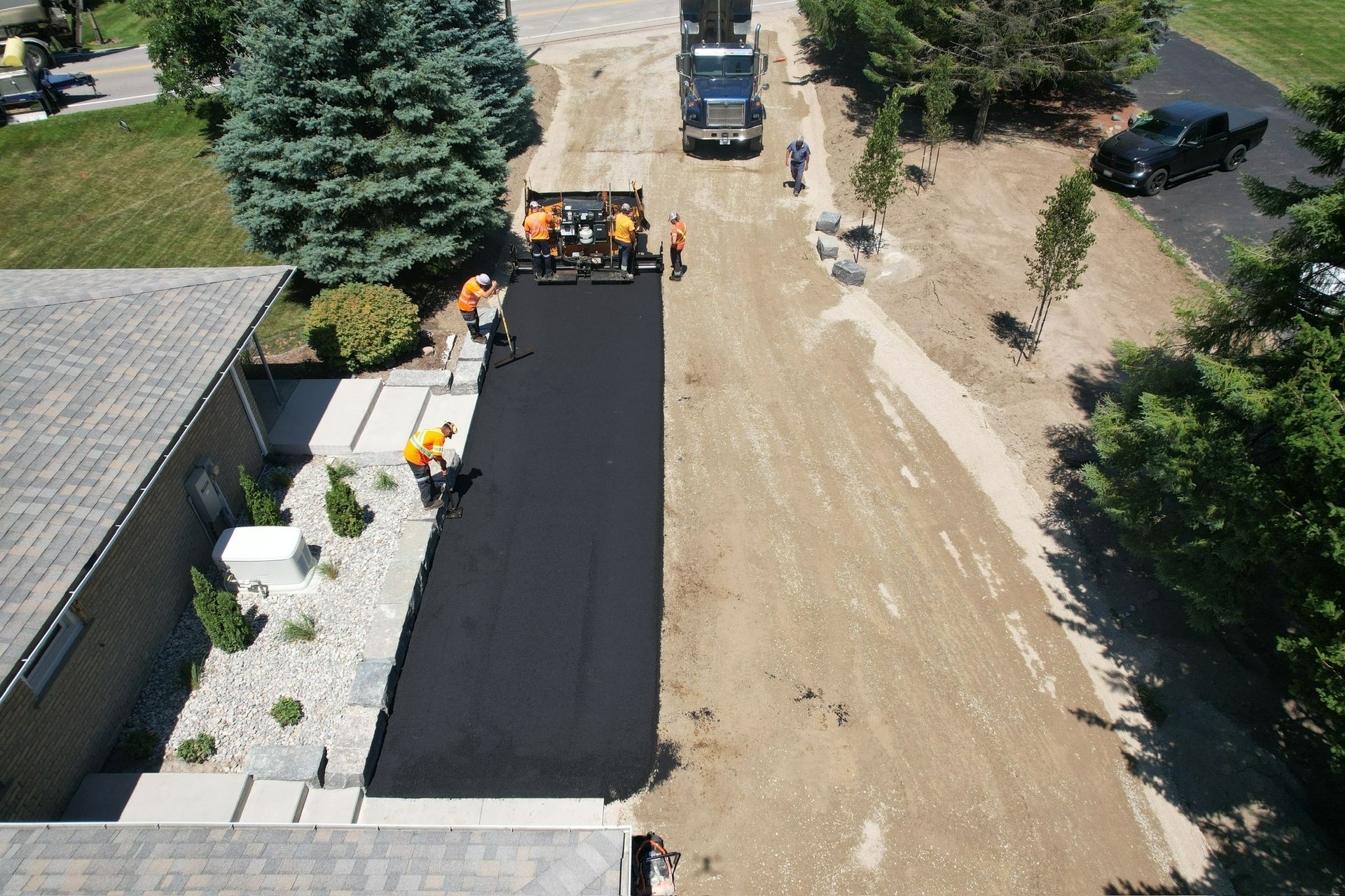 An aerial view of construction workers paving a black asphalt driveway next to a residential house.