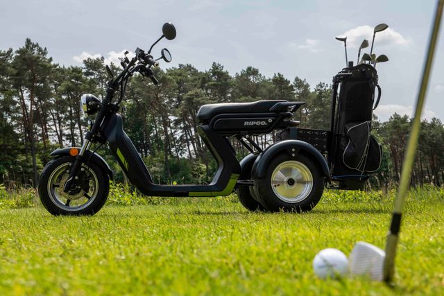 Golfkarretje op een golfbaan. Zwart-groen scootertje met een golftas, op het gras met een golfbal en tee.