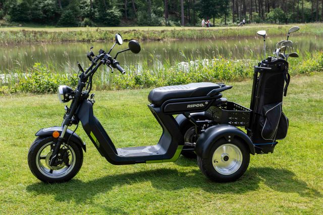 Golfkarretje op een golfbaan. Zwart-groen scootertje met een golftas, op het gras met een golfbal en tee.
