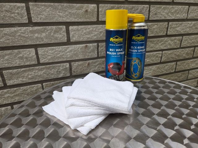 Twee spuitbussen en opgevouwen witte doeken op een metalen tafel voor een bakstenen muur.