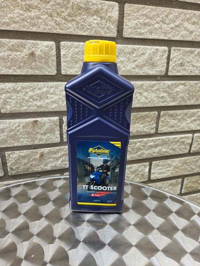 Blauwe fles scooterolie met gele dop, tegen een bakstenen muur.
