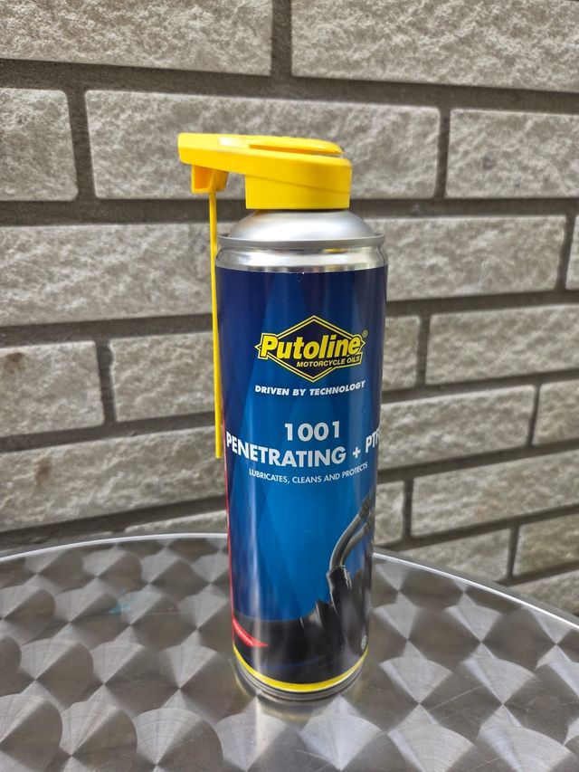 Een bus Putoline 1001 kruipolie met gele spuitmond, tegen een bakstenen muur.