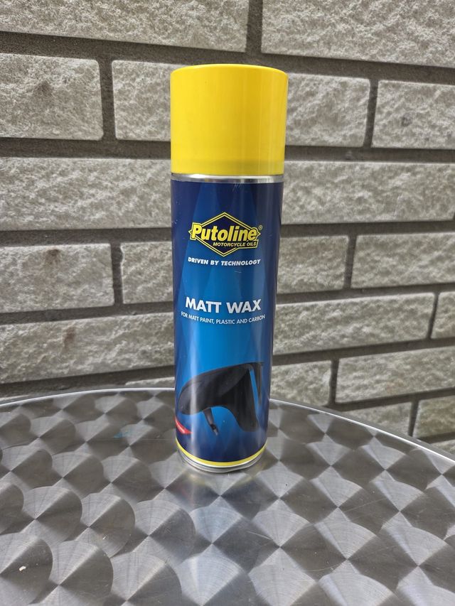 Een blik Autoline Matt Wax staat op een zilverkleurige tafel voor een bakstenen muur. Het blik is blauw, geel en transparant.