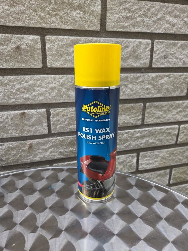 Een geel-blauwe spuitbus Putoline RS1 waxpolish staat op een tafel voor een bakstenen muur.