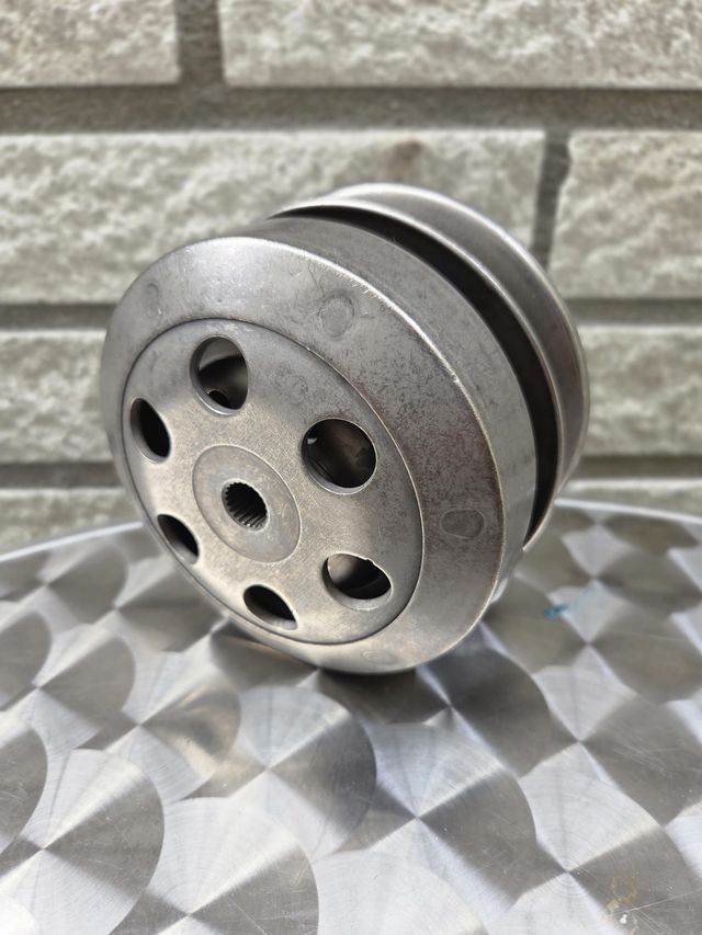 Metalen katrol met meerdere cirkelvormige niveaus en een gatenpatroon, op een gestructureerd oppervlak.