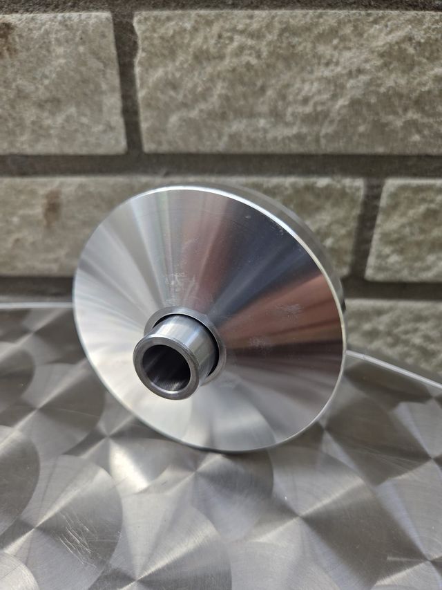 Een scootervariator met beige rollen en een metalen tandwiel op een glanzend oppervlak, tegen een bakstenen muur.