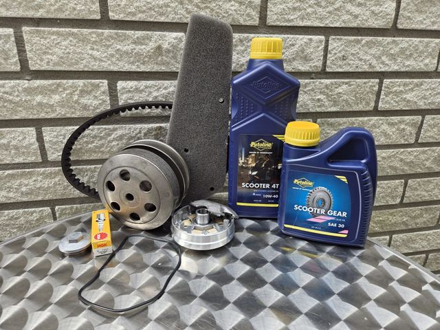 Scooteronderdelen: riem, variator, bougie, olie, filter en koppelingsonderdelen op een tafel.