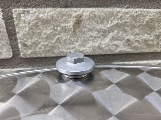 Zilverkleurige boutkop en sluitring op een geborsteld metalen oppervlak, tegen een lichtgekleurde bakstenen muur.