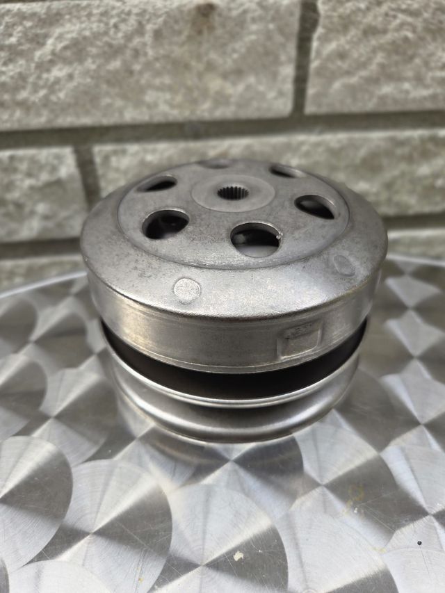 Metalen katrol met meerdere cirkelvormige niveaus en een gatenpatroon, op een gestructureerd oppervlak.