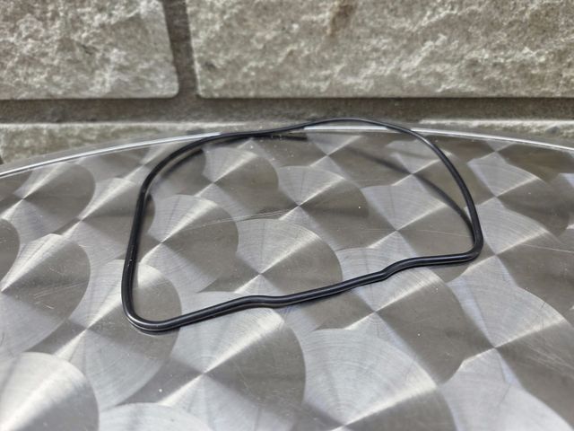 Zwarte rubberen pakking op een zilverkleurig, gestructureerd oppervlak, voor een grijze bakstenen muur.