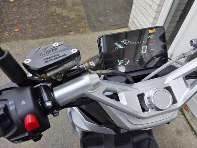 Een zwarte en grijze driewielige scooter met groene accenten staat geparkeerd voor een gebouw met glazen deuren.