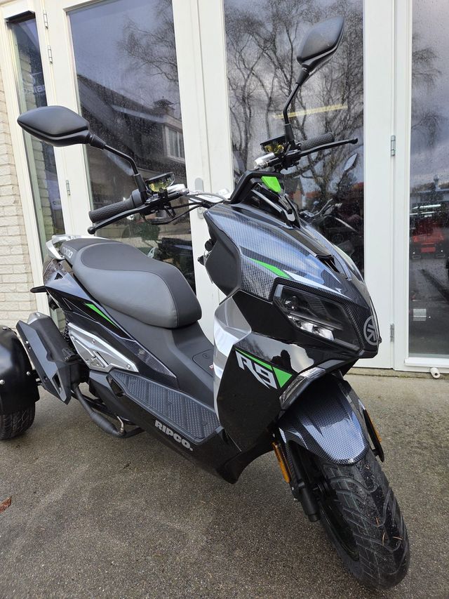 Een zwarte en grijze driewielige scooter met groene accenten staat geparkeerd voor een gebouw met glazen deuren.