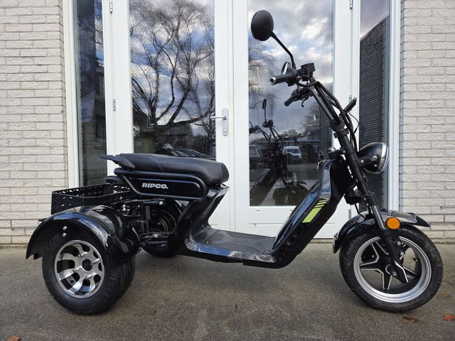 Een zwarte driewielige scooter staat geparkeerd voor glazen deuren; hij heeft een zadel, een stuur en een laadruimte.